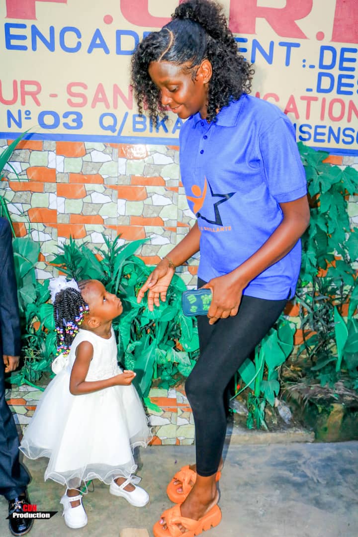Une bénévole de l'AFOREB avec une petite fille devant la pancarte de la fondation